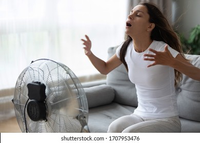 Overheated Woman Enjoying Fresh Air, Cooling Herself By Electric Fan Close Up, Exhausted Tired Pretty Girl Sitting On Couch In Front Of Ventilator, Suffering From Hot Summer Weather At Home