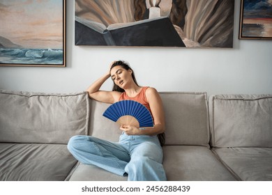 Overheated woman sits on couch in living room at hot summer weather day feel discomfort suffers from heat waving blue fan to cool. Exhausted girl artist sweating cannot working without air conditioner - Powered by Shutterstock