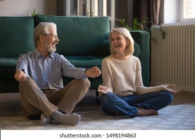 Overjoyed Active Elderly Husband And Wife Sit On Floor With Mudra Hands Practice Yoga At Home, Smiling Senior 60s Couple Meditate Relieve Negative Emotions, Healthy Lifestyle, Stress Free Concept