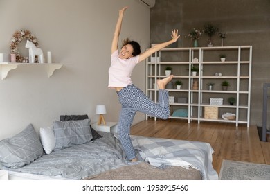Overjoyed active young latin lady having fun in bedroom jump on firm comfortable mattress. Funny teen female dance on bed enjoy good happy life excited with new flat modern renovated interior design