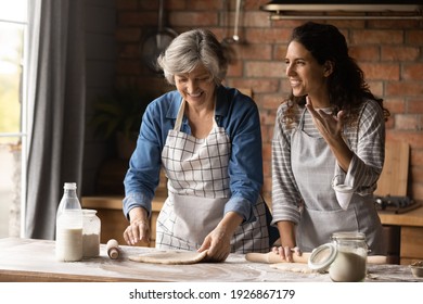 Overjoyed adult Hispanic girl with senior mom make dough bake cookies pastries together on weekend. Happy millennial Latino woman with mature mother have fun cooking dessert at home kitchen.
