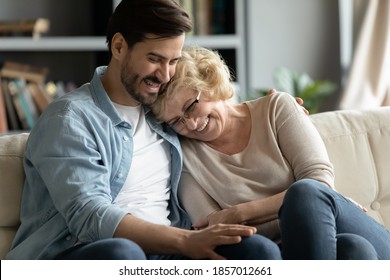 Overjoyed Adult Son And Mature Mother Hugging, Having Fun, Relaxing On Couch Together, Excited Young Man And Elderly Woman Wearing Glasses Laughing, Chatting, Enjoying Leisure Time At Home