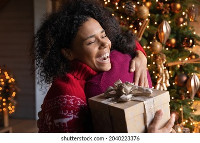 Overjoyed African American Couple Hug Exchange Christmas Presents On Winter Holidays At Home. Happy Millennial Biracial Man And Woman Embrace Celebrate New Year Make Presents. Celebration Concept.