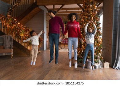 Overjoyed African American Family Jumping Near Christmas Tree, Enjoying Winter Holidays At Home, Happy Mother And Father With Son And Daughter Having Fun, Laughing And Dancing, Flying In Air