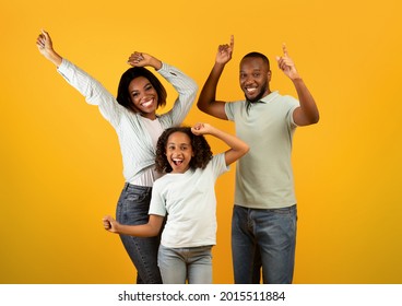 Overjoyed African American Family Of Three Dancing And Enjoying Favorite Music Together On Yellow Studio Background. Happy Black Parents Having Fun With Their Daughter