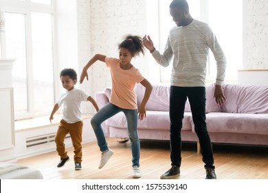 Overjoyed African American Father Have Fun Dancing With Small Preschooler Kids In Living Room At Home, Happy Biracial Dad Engaged In Funny Activity, Relax Enjoy Leisure Weekend With Little Children