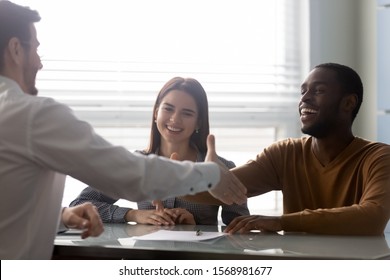 Overjoyed african American husband handshake male realtor or broker happy to sign contract buy house, excited multiethnic couple shake hands with agent closing deal or making successful agreement - Shutterstock ID 1568981677