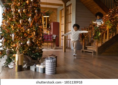 Overjoyed African American little kids wearing sweaters running downstairs on Christmas morning to opening presents, gift boxes under decorated festive tree, excited girl and boy celebrating New Year - Powered by Shutterstock