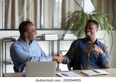 Overjoyed African American male business partners shake hands close deal after success office negotiation. Smiling biracial businessmen handshake get acquainted greet at meeting. Partnership concept.