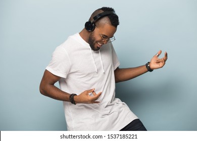 Overjoyed African American Millennial Man In Modern Earphones Isolated On Blue Studio Background Have Fun Play Imaginary Guitar, Excited Biracial Man In Headphones Listen To Music Dancing