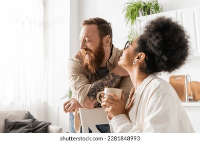 Overjoyed african american woman holding coffee cup near bearded boyfriend at home - Shutterstock ID 2281848993