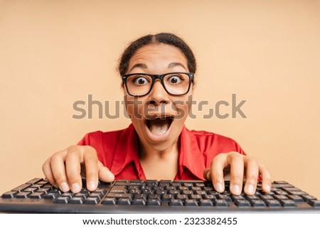 Overjoyed African American woman typing on keyboard shopping online with sale, ordering food isolated on beige background. Excited modern female playing video game with open mouth. Innovation concept