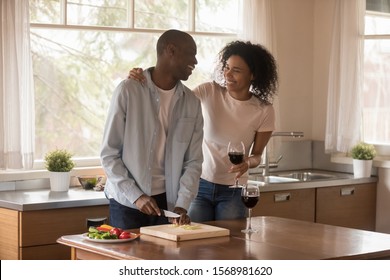 Overjoyed african American young family relax in kitchen together, drink wine preparing cooking food, smiling happy biracial millennial husband and wife enjoy romantic date or weekend at home - Powered by Shutterstock