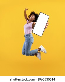 Overjoyed african american young lady showing empty smartphone screen while jumping up over yellow studio background, collage, full size photo. Happy black woman recommending new mobile app