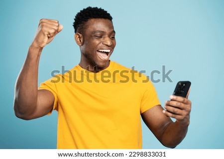Overjoyed African man using smartphone sports betting, win money isolated on blue background. Emotional Nigerian gambler playing mobile game celebration success. Hipster male shopping online with sale