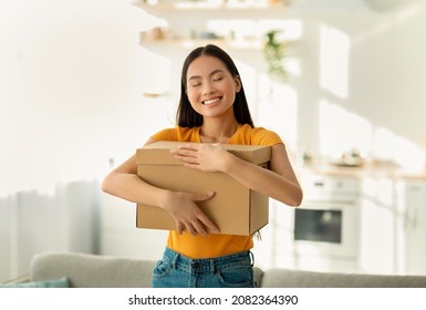 Overjoyed Asian Lady Hugging Carton Parcel, Receiving Long Awaited Delivery, Getting Online Order, Standing At Home. Satisfied Female Customer Empracing Her Internet Purchase In Cardboard Package