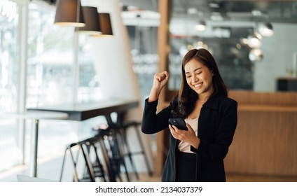 Overjoyed Asian woman reading good news, holding phone, celebrating success or online lottery win, job promotion, excited businesswoman showing yes gesture, laughing.