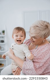 overjoyed baby girl holding spoon near smiling grandmother in kitchen