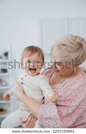 overjoyed baby girl holding spoon near smiling grandmother in kitchen