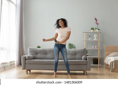 Overjoyed black biracial millennial girl dancing alone moving to rhythm in living room, happy african American young woman have fun enjoying listening to music, entertain on weekend at home - Powered by Shutterstock