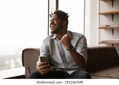 Overjoyed Black Male Hipster Blogger Receive Perfect Commercial Offer Pleasant Comment At Social Network. Excited Young African Man Watch Lottery Result On Smartphone Screen Celebrate Winning Jackpot