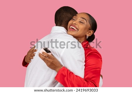 Overjoyed black woman in red embracing man, showing off her new engagement ring behind his back, moment of pure happiness, pink background