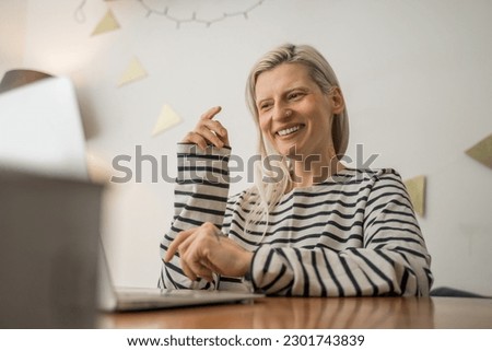 Overjoyed blonde woman sitting at the kitchen and laughing while talking via video call