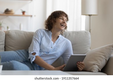 Overjoyed Caucasian female relax on sofa at home have fun suing tablet shopping online. Smiling young woman rest on couch in living room browse surf wireless internet on pad. Technology concept. - Shutterstock ID 1911357664