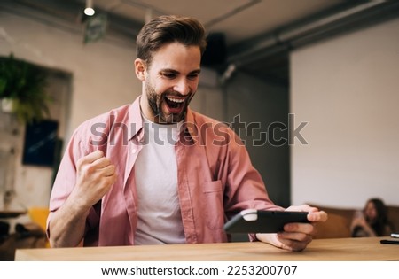 Overjoyed Caucasian male celebrating victory in online contest using modern joypad technology, excited millennial man rejoicing while winning video game level on console controller during free time