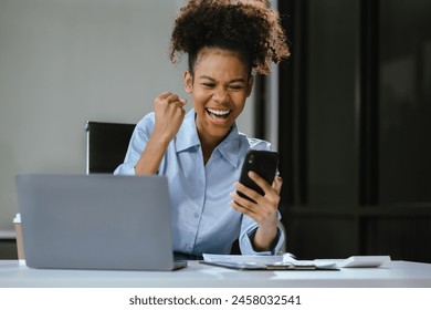 Overjoyed charming excited black woman business woman worker using smartphone and laptop working in office, feeling happy. - Powered by Shutterstock