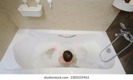The overjoyed child enjoys a bubble bath with toys. Happily seated in the water, the little one has fun splashing around. Kid about two years old (one year ten months).