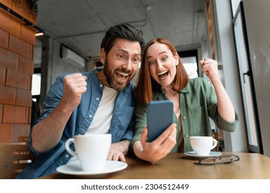 Overjoyed couple of friends holding mobile phone shopping online with sales, win money, celebration success sitting in modern cafe. Happy successful freelancers receive payment, reading good news  - Shutterstock ID 2304512449