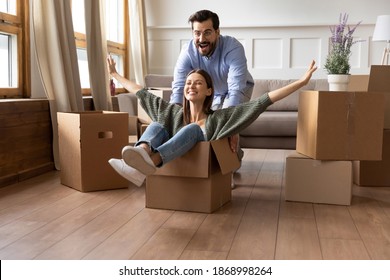 Overjoyed couple renters have fun ride in cardboard box relocate at new home together. Happy man and woman tenants engaged in funny activity feel playful on moving day. Relocation, rental concept.
