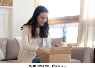 Overjoyed curious young woman opening cardboard box with goods, awaited parcel at home, sitting on couch, satisfied client received online store order, good quick delivery service concept
