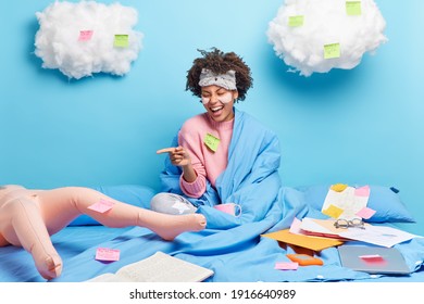 Overjoyed Curly Woman Has Upbeat Mood Points At Inflated Doll Has Imaginary Friend Stays In Bed Works On Freelance Project Enjoys Cozy Domestic Atmosphere Covered With Blanket Feels Comfortable