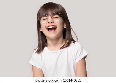 Overjoyed cute small preschooler girl in glasses isolated on grey studio background feel happy laugh at funny joke, smiling little child in spectacles excited with good sight correction at opticians
