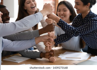 Overjoyed diverse multiracial young people stack fists engaged in funny teambuilding activity at group meeting, excited multiethnic students build strong cooperation show unity support at gathering