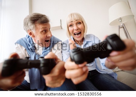 Overjoyed elder couple playing video games with joystick, having fun at home