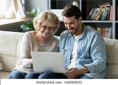 Overjoyed elderly mother sit rest on sofa with grown-up son watch funny video on modern laptop, happy middle-aged mom rest in living room with adult child use computer enjoy family weekend together