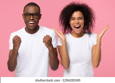 Overjoyed excited african american family couple winners celebrate win enjoy victory rejoice success, happy ecstatic euphoric black man and woman screaming with joy isolated on pink studio background