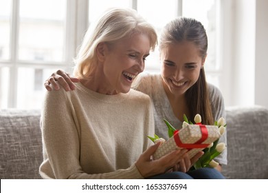 Overjoyed Excited Curious Mature Woman Sitting With Bonding Grown Up Happy Smiling Daughter On Sofa, Holding Looking At Unexpected Surprise, Wrapped Gift Box, Trying Guess What’s Inside Head Shot.