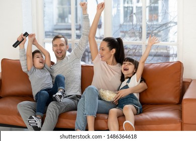 Overjoyed Excited Family Football Fans Watching Sport Tv Celebrating Goal, Happy Euphoric Parents And Cute Little Children Kids Screaming Supporting Favorite Soccer Team Victory At Home Sit On Sofa