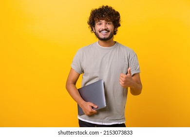 Overjoyed Excited Indian Man Showing Big Finger And Holding Laptop While Looking At Camera With Happy Smile. Indoor Studio Shot Isolated On Yellow Background