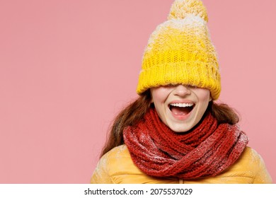 Overjoyed excited jubilant young woman 20s wears yellow jacket hat mittens cover close hiding eyes with hat cap keeping mouth wide open isolated on plain pastel light pink background studio portrait