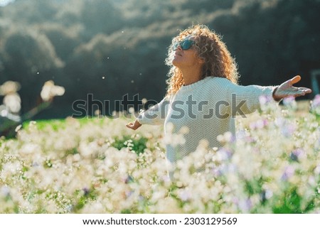 Overjoyed and excited young lady opening arms outstretching in a white flowers blossom meadow. Summer outdoor leisure activity. One woman enjoy nature park. Happiness and healthy lifestyle people