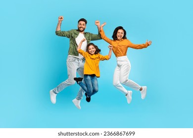 Overjoyed family of three jumping gesturing yes and smiling, parents and daughter posing together in mid air over blue studio background, full length - Powered by Shutterstock