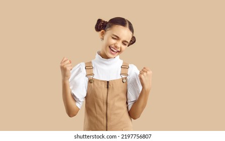 Overjoyed funny Caucasian girl teenager experiencing positive emotions making hand gestures as sign of victory with eyes closed in happiness dressed in casual clothes stands in beige studio - Shutterstock ID 2197756807