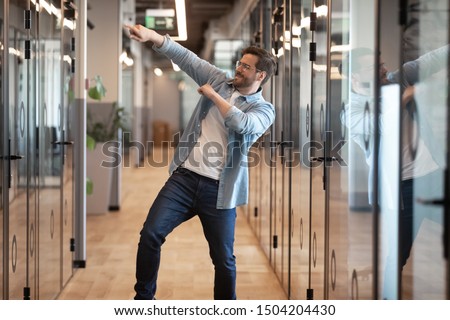 Overjoyed funny male employee have fun perform winner dance in modern office hallway, excited happy millennial businessman celebrate business success or promotion, Friday evening, end of working week