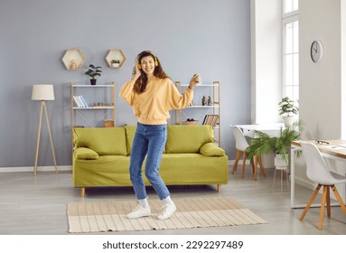 Overjoyed girl wearing headphones listening to music and dancing. Happy positive girl in casual clothes having fun and relaxing in living room at home. Woman enjoying music and leisure weekend