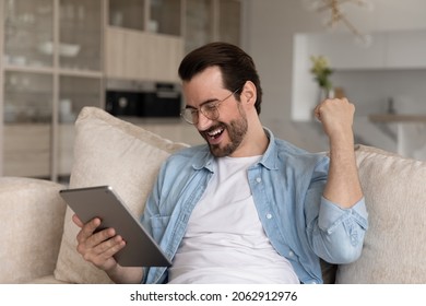 Overjoyed handsome millennial man in eyewear looking at touchpad gadget screen, celebrating online lottery results, feeling excited of getting email with auction betting giveaway win at home. - Shutterstock ID 2062912976